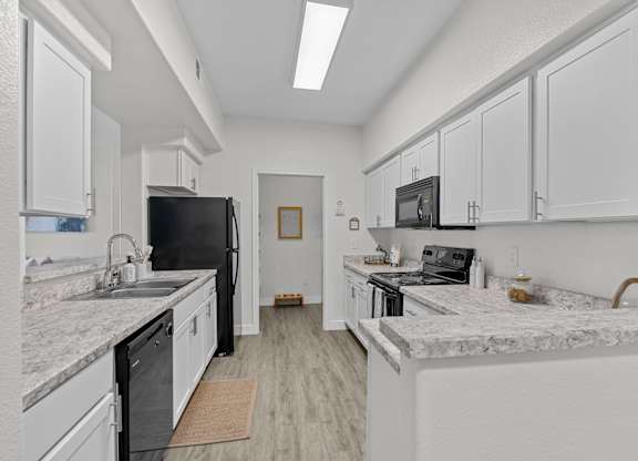 A kitchen with a black refrigerator and white cabinets.