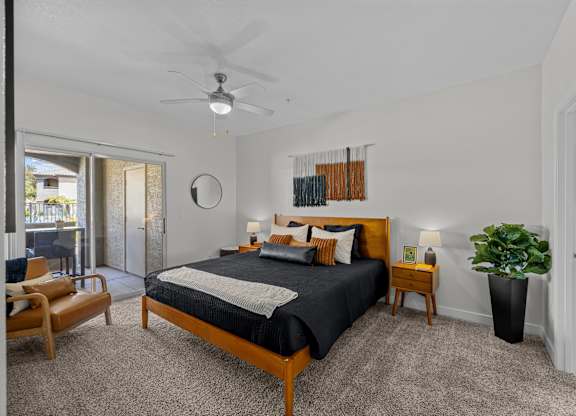A bedroom with a bed, nightstand, chair, and plant.