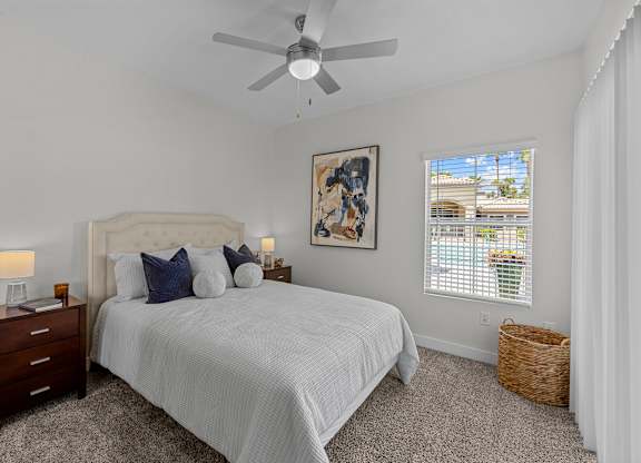 A bedroom with a large bed, a ceiling fan, and a window with blinds.