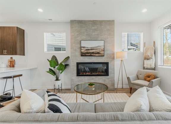 A modern living room with a grey sofa, a glass coffee table, and a fireplace.