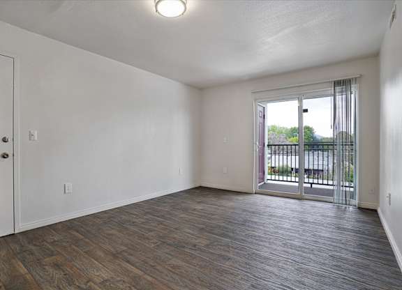 A room with a white door and a window with a view of a fence and trees.