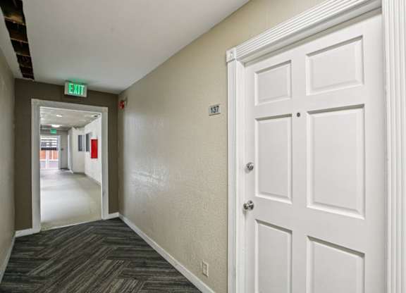 A hallway with a white door and a green exit sign.