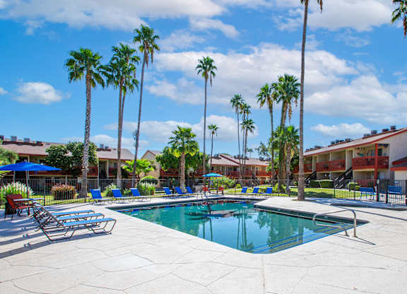 A pool surrounded by palm trees and lounge chairs.