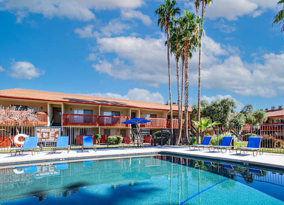 A swimming pool in front of a building with palm trees.