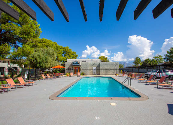 A large swimming pool surrounded by orange lounge chairs and wooden pergolas.