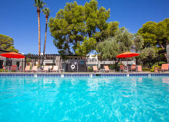 A swimming pool surrounded by trees and chairs with umbrellas.