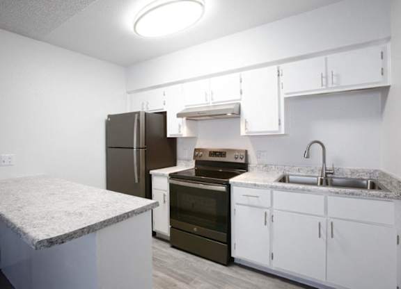 A kitchen with a refrigerator, oven, and sink.