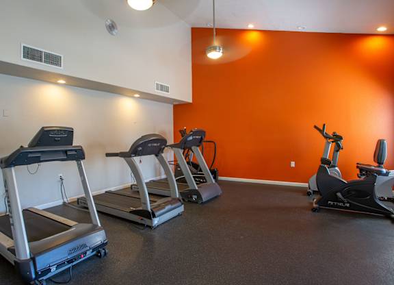 A gym with orange walls and treadmills.