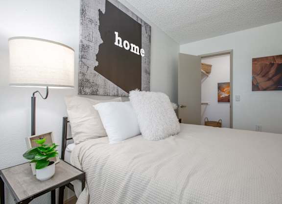 A bedroom with a bed, lamp, and a picture of a woman.
