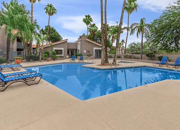 A pool surrounded by palm trees and a house in the background.