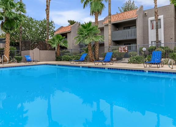 A swimming pool surrounded by palm trees and lounge chairs.