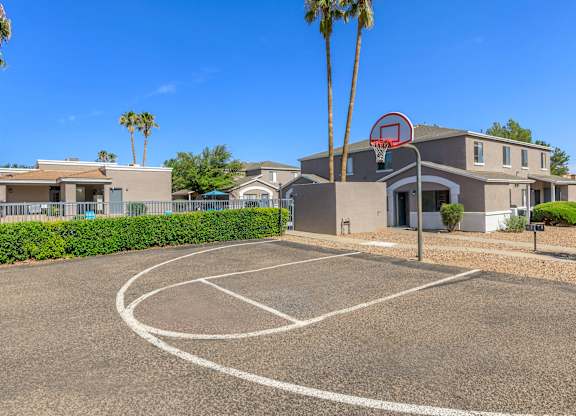 A basketball court is located in front of a building with a basketball hoop.