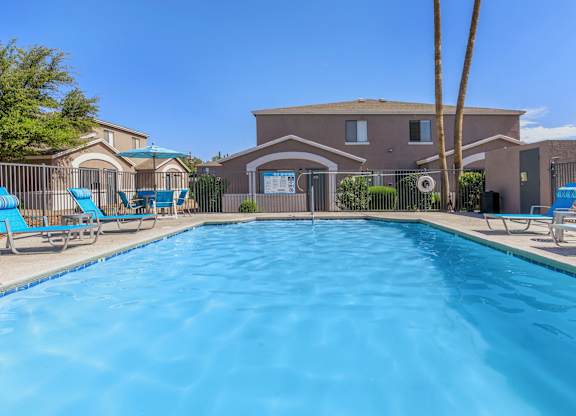 A swimming pool in front of a house with a fence and palm tree.