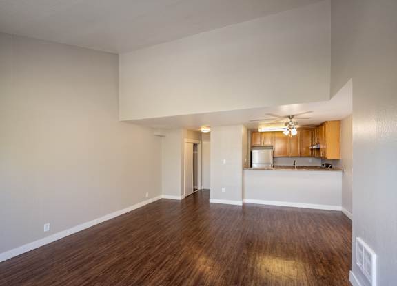 A large empty room with wooden floors and a kitchen area in the background.