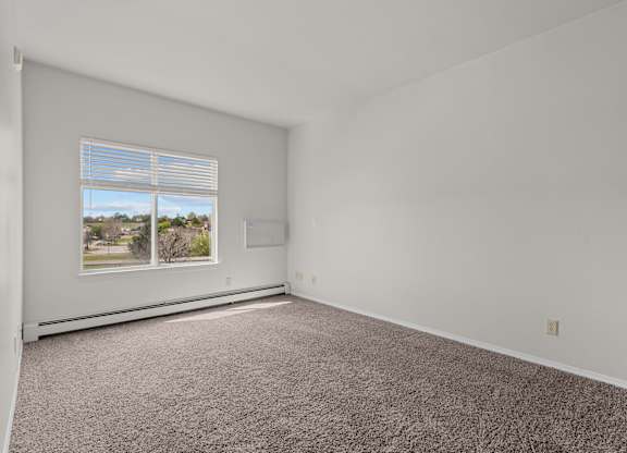 A room with a carpeted floor and a window with blinds.