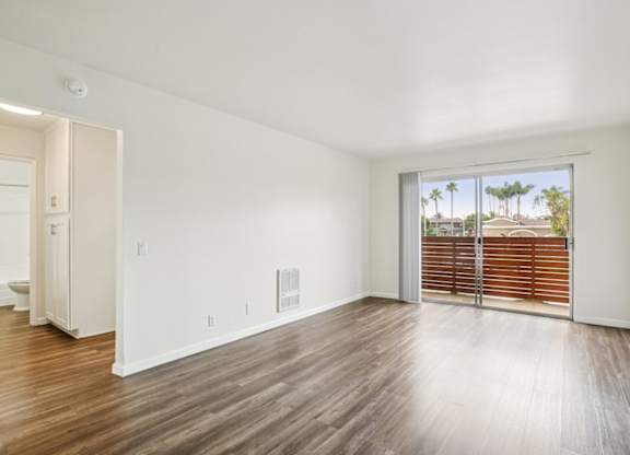 A room with wooden floors and a sliding glass door leading to a balcony.