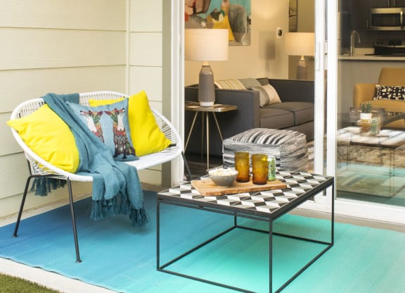 a patio with a white chair and a coffee table on a blue rug