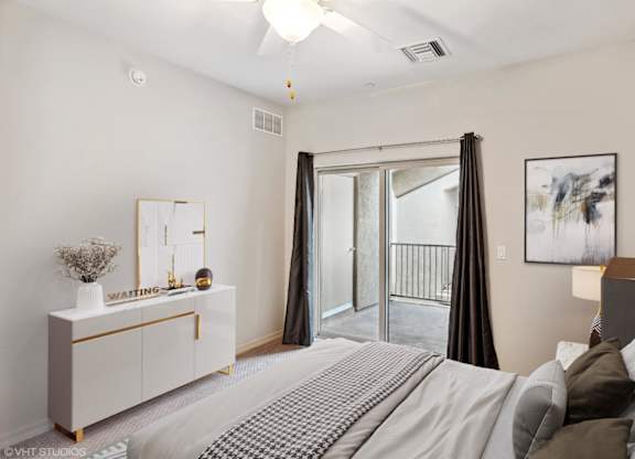 A bedroom with a large bed, a dresser, and a balcony.