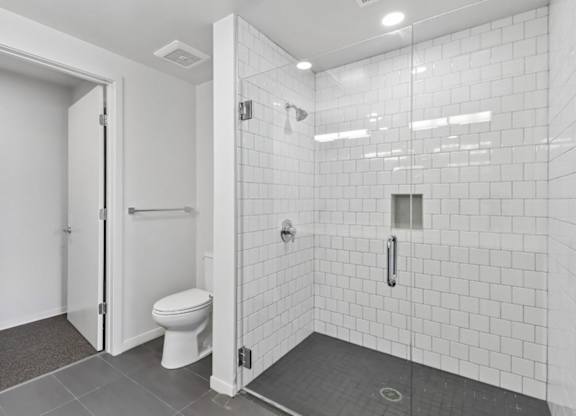 A white tiled bathroom with a toilet and a walk-in shower.