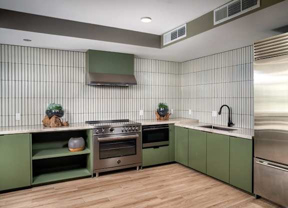 A modern kitchen with green cabinets and stainless steel appliances.