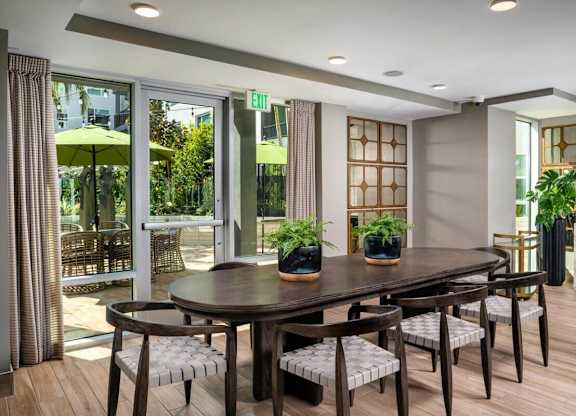 A dining room with a table and chairs and a window with a view of the outside.