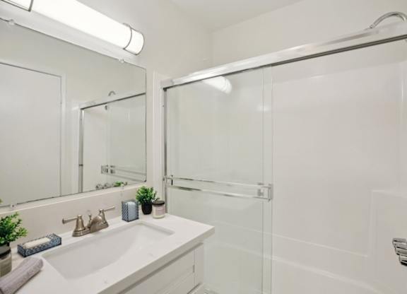 A white bathroom with a sink, mirror, and shower.