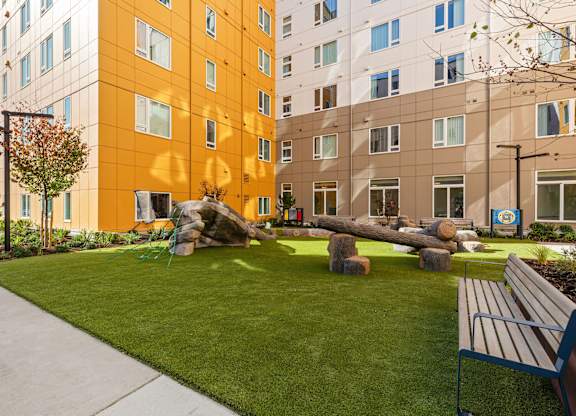 A park area with a bench and a tree in front of a building.