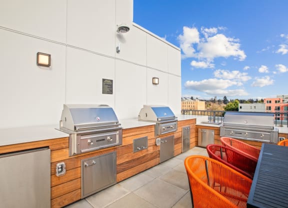 the cookout area of a rooftop patio with barbecue grills and chairs