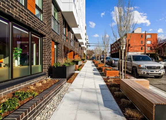 a sidewalk in front of a building with benches and plants