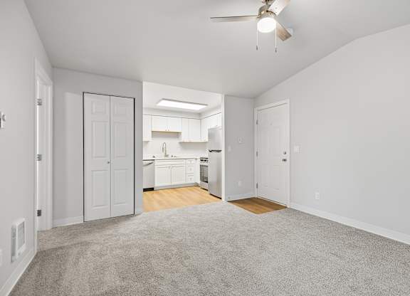 A spacious, empty room with a carpeted floor and a ceiling fan.