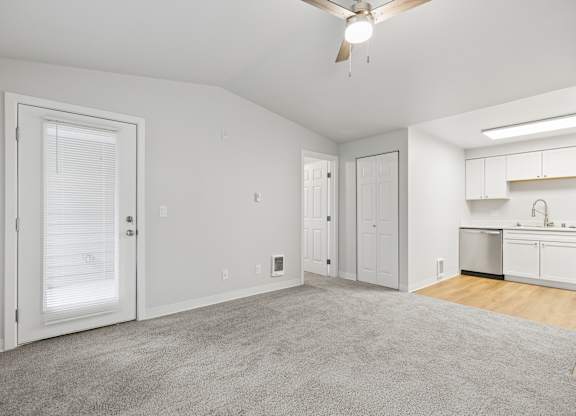 A spacious living room with a ceiling fan and a kitchen area in the background.
