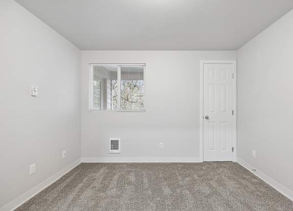 A room with a carpeted floor and a window with blinds.
