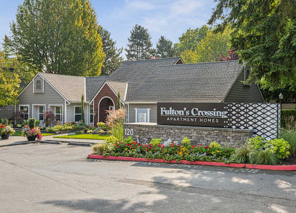 A sign for Fulton's Crossing Apartment Homes is in front of a house.