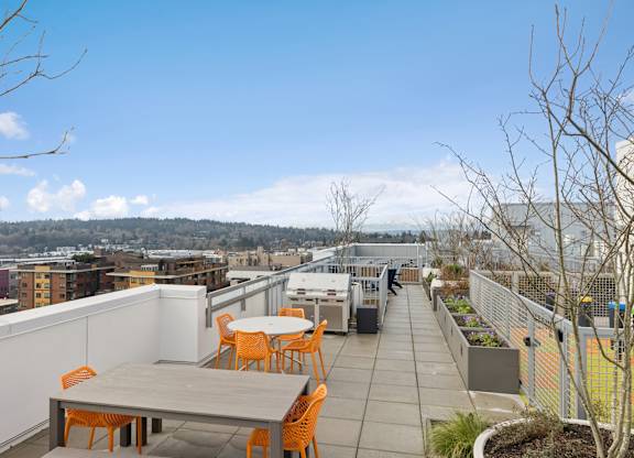 A rooftop patio with a table and chairs overlooking a cityscape.