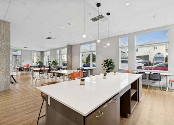 A large white counter with orange chairs in a room with a lot of windows.