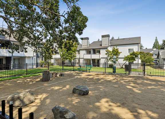 A playground area with a sandbox and rocks in the foreground and a building in the background.