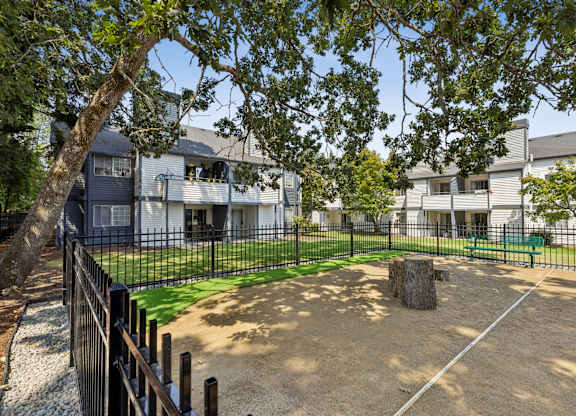 A playground area with a sandbox and a fence in front of a building.