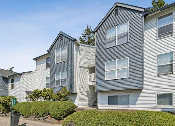 A grey apartment building with a green bush in front.
