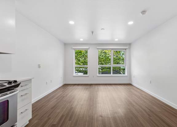 A white room with a wood floor and a window with a view of trees.