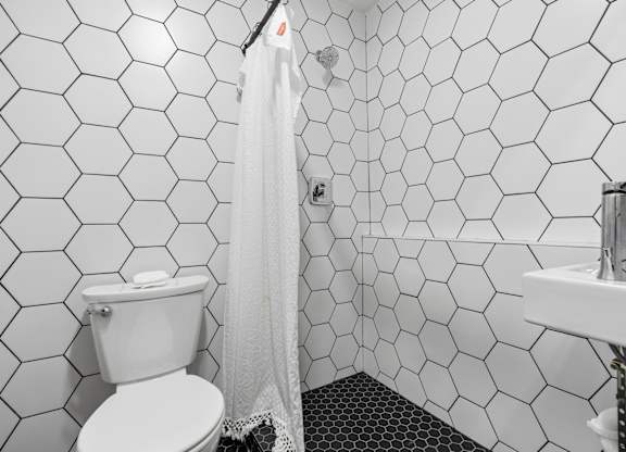 A white toilet with a white shower curtain in a bathroom with hexagonal tiles.
