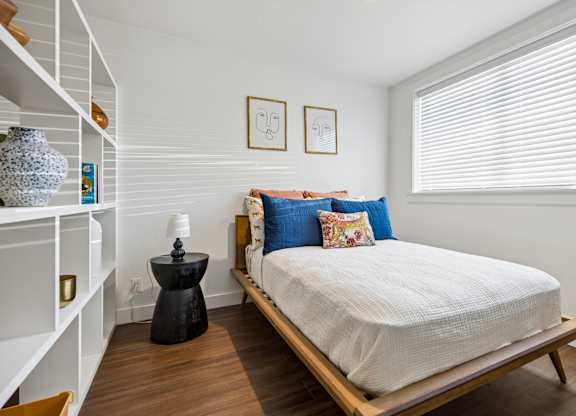 A bedroom with a bed, nightstand, and shelves.