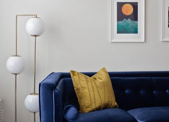 A blue couch with a yellow pillow and a white floor lamp.