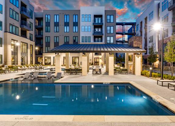 A large swimming pool in front of a building with a sun lounger and a table.