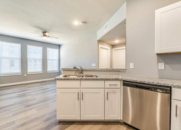 A kitchen with a stainless steel dishwasher and white cabinets.at Four Cedars, Gunter, TX