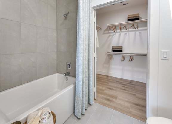 A white bathroom with a tub and a walk in closet.