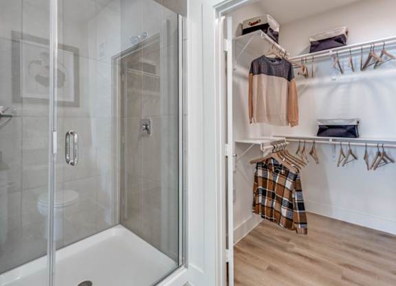 A bathroom with a walk-in shower and a closet with clothes hanging.