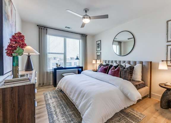 A bedroom with a large bed, a ceiling fan, and a mirror on the wall.