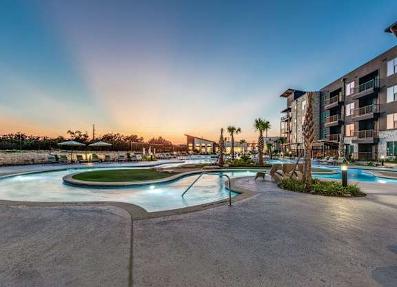 A large outdoor swimming pool surrounded by a concrete patio and a building in the background.
