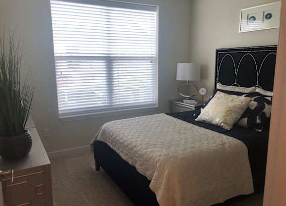 A bedroom with a bed, nightstand, and window with blinds.