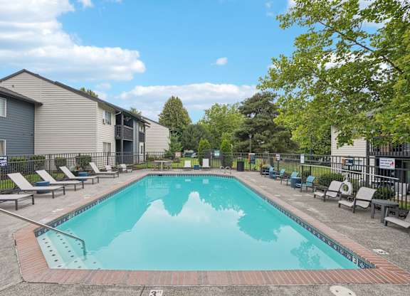 A swimming pool surrounded by lounge chairs and trees.